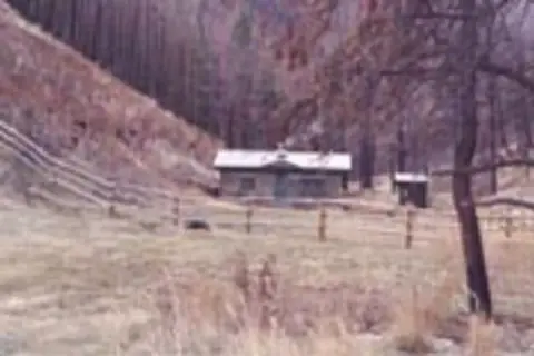 A small cabin sits in a valley near a hillside.