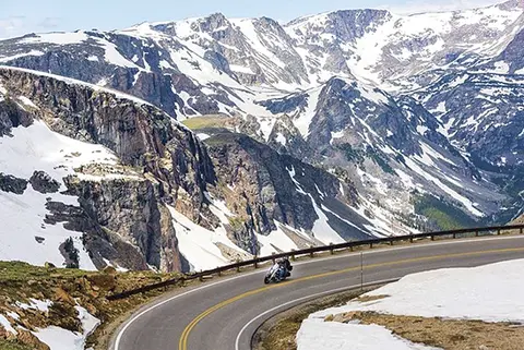 A motorcyclist rides along a winding road through snowy mountains.