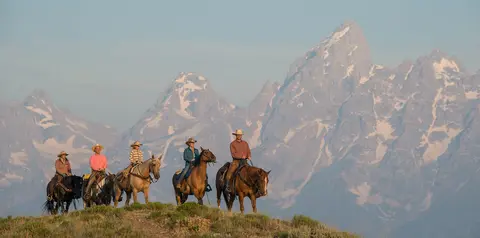 People horseback riding in front of a mountain range.
