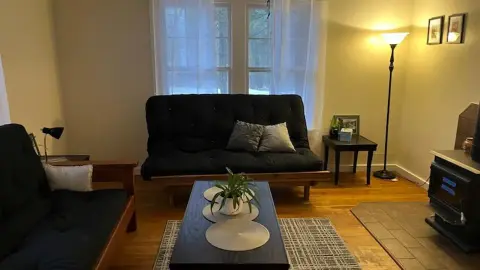 An interior view of a cozy living room with a black futon and a wood stove.