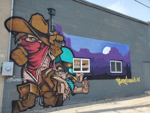 A colorful mural of a cartoon cowboy is painted on the exterior brick wall of a building.