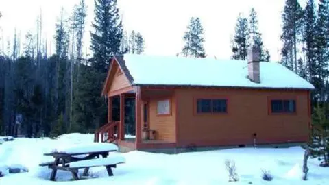 A cabin covered in snow in a wooded area.