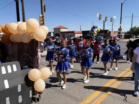 A group of cheerleaders walking in a parade next to a float decorated with balloons.