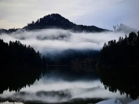 A scenic landscape featuring a forested mountain and low-lying clouds reflecting in a calm body of water.