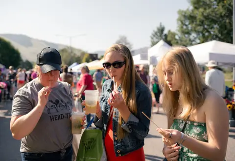 Three people stand outside at an event drinking from cups with straws.