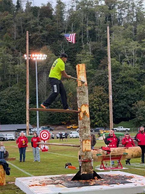 A competitor chops a tall log standing on a springboard.