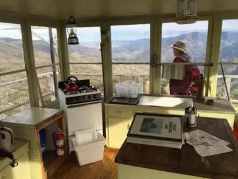 The interior of a fire lookout tower overlooking a mountainous landscape with a person looking out the window.