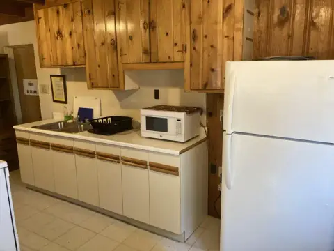 A kitchen interior features wooden cabinets, white countertops, a microwave, and a white refrigerator.