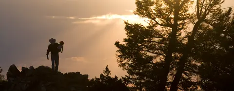 A silhouette of a person holding a child on a rocky hill during sunset.