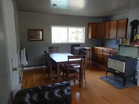 A rustic kitchen and dining area with wooden floors, wooden cabinets, a dining table, and a wood stove.
