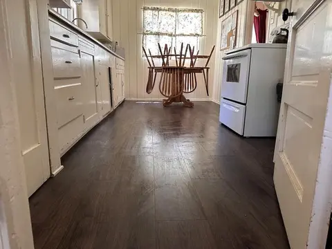 A view of a rustic kitchen with dark wood flooring, white cabinets, and a dining table with chairs flipped upside down on it.