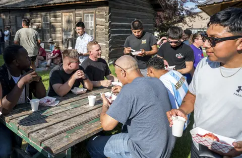 A group of people sitting at outdoor picnic tables eating food.