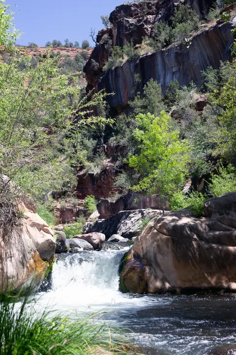 A small waterfall flowing through a rocky canyon with trees and cliffs in the background.