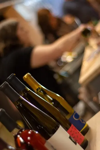 Several wine bottles rest on a counter while people work in the background.