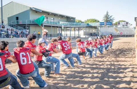A team of people in red jerseys participate in a tug-of-war competition on a dirt field.