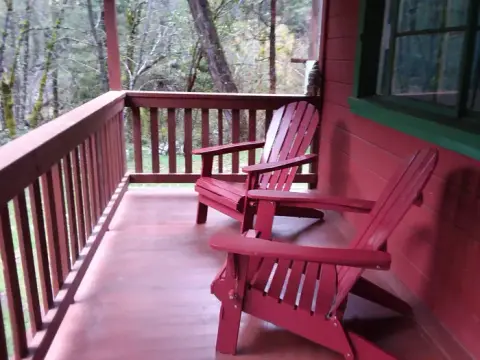 Two red chairs sit on a wooden porch outside a building.