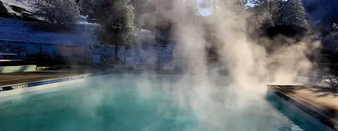 Steam rises from an outdoor swimming pool set against a snowy hillside.