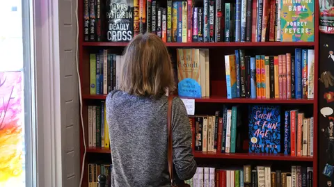 A person browsing books on a bookshelf inside a shop.