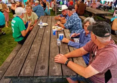 People sit around a wooden picnic table outdoors at an event.
