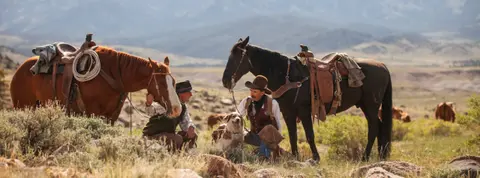 Two cowboys with horses and a dog in a landscape.