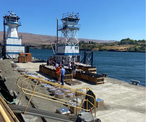 People working near boats and stacked boxes on a dock by a river.