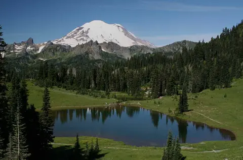 A scenic landscape featuring a snow-capped mountain overlooking a forested lake.