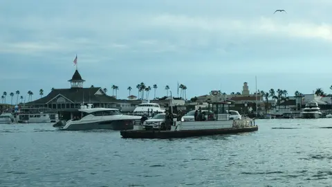 A ferry boat carrying cars and passengers on a harbor with buildings in the background.