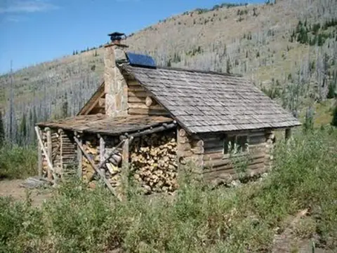 A log cabin nestled in a mountainous landscape with stacked firewood.