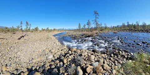 A rocky river flowing through a sparse landscape under a clear blue sky.