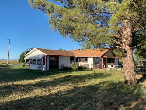A single-story white house with a brown roof stands in a grassy yard under a blue sky.