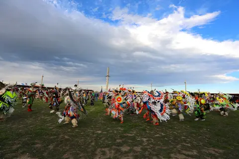 People in colorful regalia dancing outdoors under a cloudy sky.