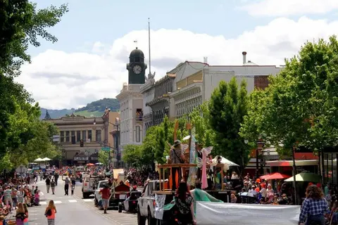 A street parade with floats and spectators in front of historic buildings.