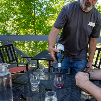 A man pours wine into a glass at an outdoor table.