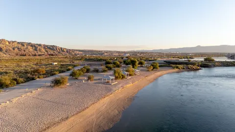 A sandy beach along a river with desert mountains in the background.