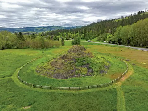 A grassy mound surrounded by a circular wooden fence in a landscape.