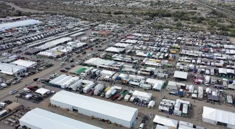 An aerial view shows a sprawling outdoor market with many tents, RVs, and vehicles.