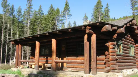 A rustic log cabin sits surrounded by tall pine trees.