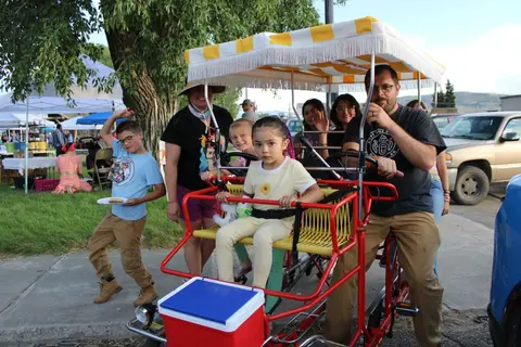 A family sitting in a multi-person pedal surrey with a yellow and white striped canopy.