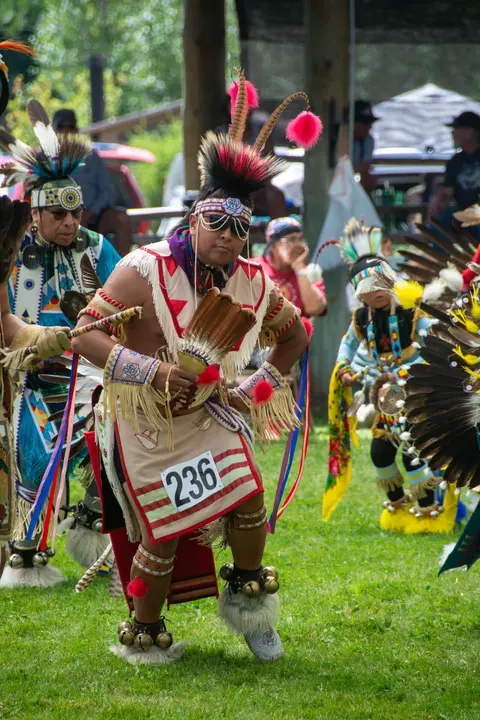 People in traditional regalia perform a dance outdoors.