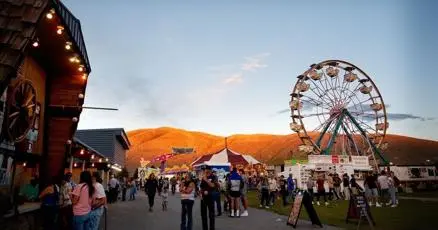 A crowd of people enjoying an outdoor fair with a Ferris wheel at dusk.