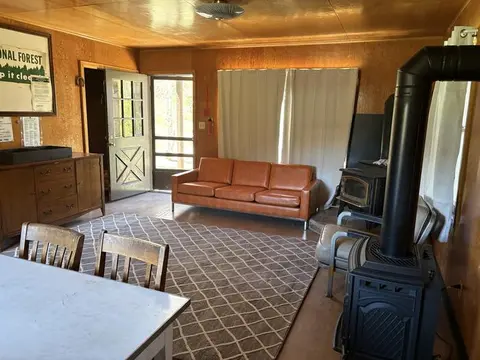 An interior view of a rustic room with wood-paneled walls, an orange sofa, and a wood-burning stove.