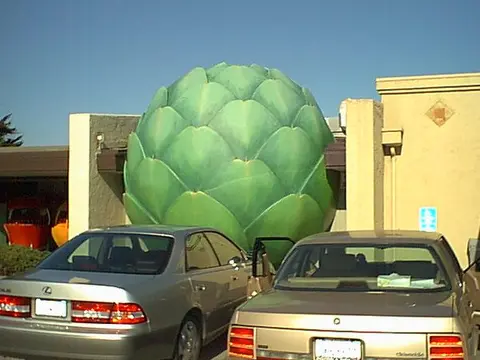 A large artichoke sculpture sits between buildings in front of parked cars.