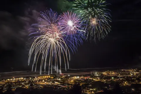 A photograph shows fireworks lighting up the night sky over a town near the coast.
