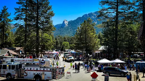 A crowd gathers along a mountain town street for a parade with a fire truck in the foreground.