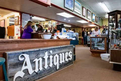 An interior view of an antiques store with a counter and customers browsing.