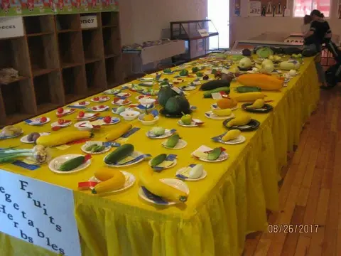 An interior shot of a long table covered in a yellow cloth displaying various fruits and vegetables.