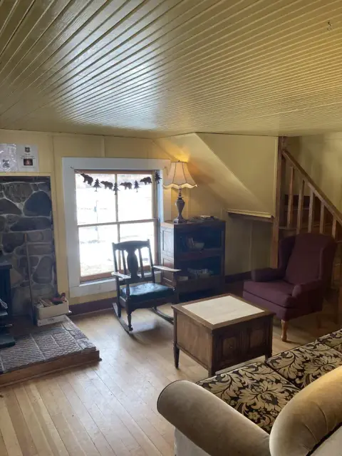 An interior view of a cozy room with wooden paneling, a fireplace, a rocking chair, and a staircase.