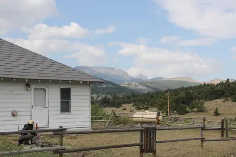 A person working near a white house with mountains in the background.