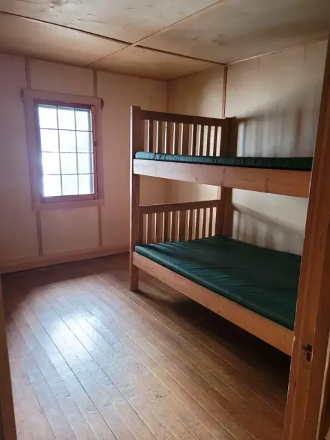 A small wooden room with a bunk bed and a window.