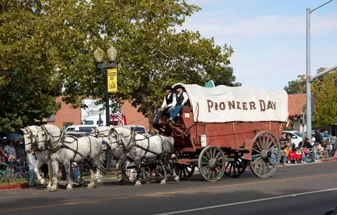 A covered wagon pulled by four horses in a parade.